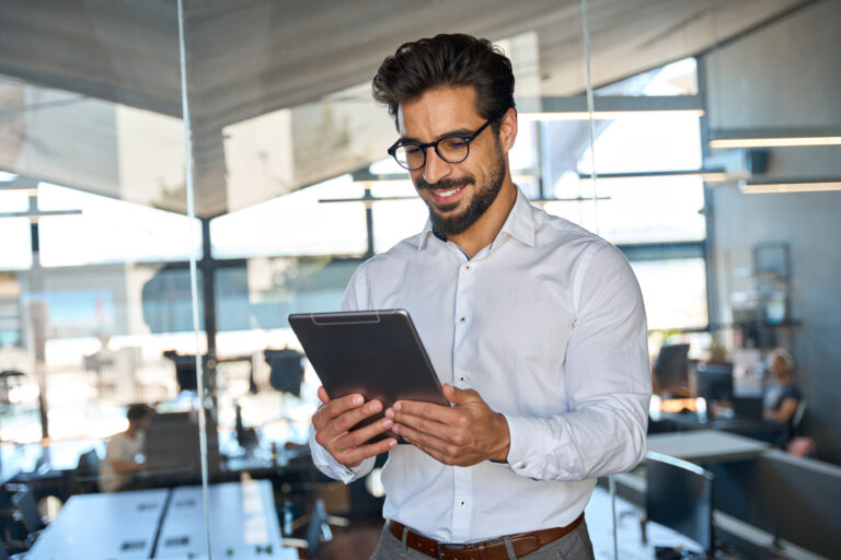 Smiling busy young Latin business man using tablet standing in office