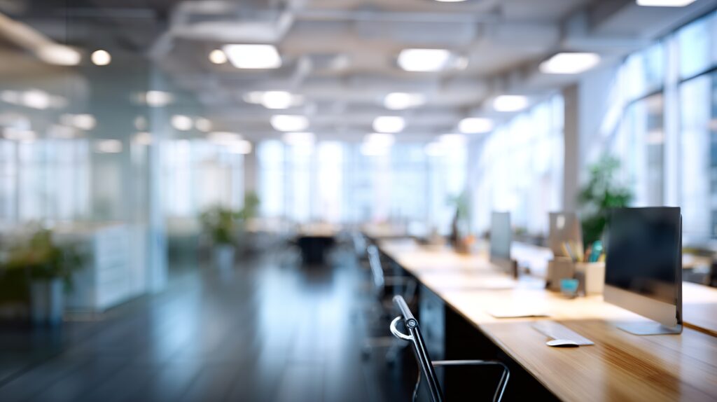 Modern open office space with desks, computers, and large windows creates a bright and spacious work environment.