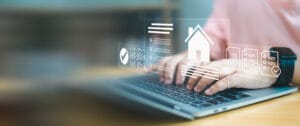 Close up of hands typing on laptop with smart home interface and digital property documents. Concept of real estate technology, online mortgage application, and digital property management.